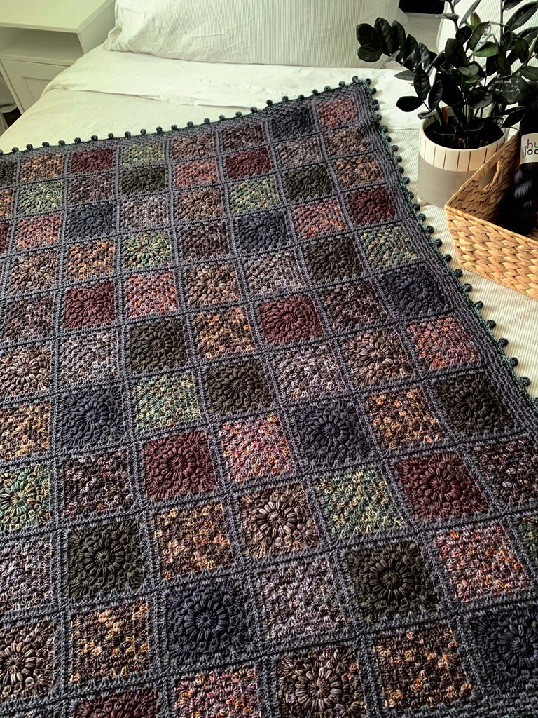 blanket on a bed, made out of semisolid speckled hand dyed dark night colors of dk yarn
